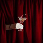 Hidden person holding a holiday martini with a red curtain behind it