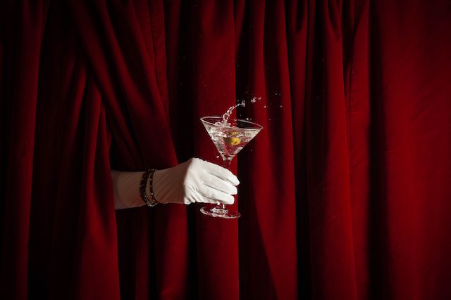 Hidden person holding a holiday martini with a red curtain behind it