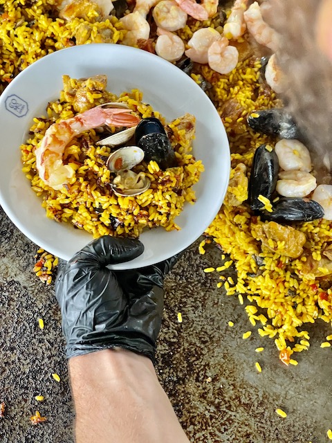 Chef holding Paella dish while being cooked outside