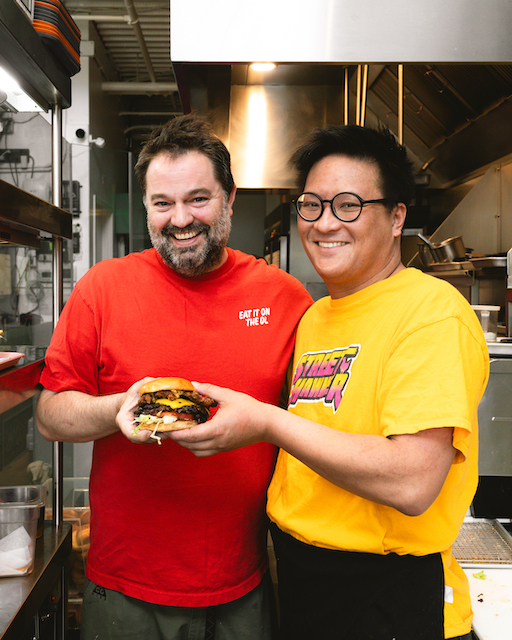 Doug Stephen and Justin Cheung holding their smash burger collaboration in kitchen