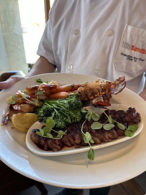 Chef holding the large plate of seafood, steak and veggies for Surf & Turf Sundays at The Sandbar