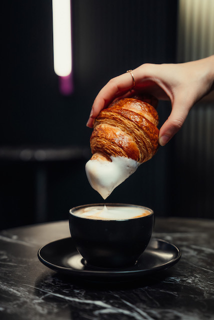 Croissant being dunked into a latte from Dolce Cafe